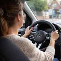 Parent au volant d’une voiture familiale équipée d’une housse de volant, avec enfants assis à l’arrière lors d’un trajet du quotidien